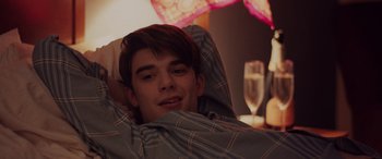 Movie still from “Alex Strangelove” (2018), directed by Craig Johnson – A man laying in bed under a blanket with a glass of wine; Close Up shot, Over the shoulder angle