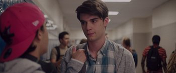 Movie still from “Alex Strangelove” (2018), directed by Craig Johnson – A young man in a plaid shirt is standing in a hallway; Close Up shot, Over the shoulder angle