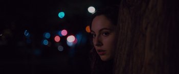 Movie still from “Alex Strangelove” (2018), directed by Craig Johnson – A woman is looking over a wooden pole at night lights; Close Up shot, Over the shoulder angle