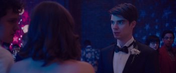 Movie still from “Alex Strangelove” (2018), directed by Craig Johnson – A man in a tuxedo talking to a woman in a black dress; Close Up shot, Over the shoulder angle