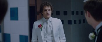 Movie still from “Alex Strangelove” (2018), directed by Craig Johnson – A man in a white suit with a rose in his lapel; Medium shot, Over the shoulder angle