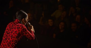 Movie still from “Ali Wong: Don Wong” (2022), directed by Nahnatchka Khan – A person holding a microphone on a stage with a crowd; Medium shot, Over the shoulder angle