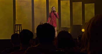 Movie still from “Ali Wong: Don Wong” (2022), directed by Nahnatchka Khan – A woman in a red and black dress holding a microphone on a stage; Wide shot, Over the shoulder angle