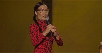 Movie still from “Ali Wong: Don Wong” (2022), directed by Nahnatchka Khan – A woman in a red leopard print dress holding a microphone; Medium shot, Over the shoulder angle