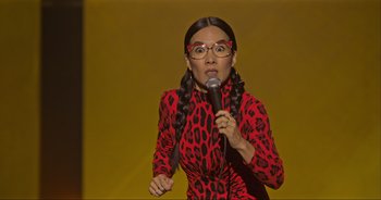 Movie still from “Ali Wong: Don Wong” (2022), directed by Nahnatchka Khan – A woman in a red and black dress holding a microphone; Medium shot, High angle