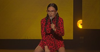 Movie still from “Ali Wong: Don Wong” (2022), directed by Nahnatchka Khan – A woman in a red dress holding a microphone and sitting on a stage; Medium shot, High angle