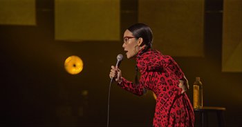 Movie still from “Ali Wong: Don Wong” (2022), directed by Nahnatchka Khan – A woman in a red dress holding a microphone; Medium shot, Over the shoulder angle