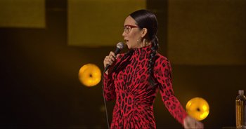 Movie still from “Ali Wong: Don Wong” (2022), directed by Nahnatchka Khan – A woman in a red dress holding a microphone; Medium shot, Over the shoulder angle
