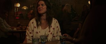 Movie still from “Alice, Darling” (2022), directed by Mary Nighy – A woman sitting at a table with two glasses; Medium shot, Over the shoulder angle