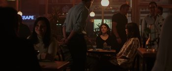 Movie still from “Alice, Darling” (2022), directed by Mary Nighy – A woman sitting at a table in front of two men; Medium shot, Over the shoulder angle