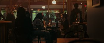 Movie still from “Alice, Darling” (2022), directed by Mary Nighy – A group of people sitting at a table in front of a window; Wide shot, Over the shoulder angle