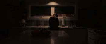 Movie still from “Alice, Darling” (2022), directed by Mary Nighy – A woman sitting at a kitchen counter in front of a window; Medium shot, Low angle