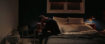 Movie still from “Alice, Darling” (2022), directed by Mary Nighy – A man sitting on top of a bed next to pillows; Medium shot, High angle