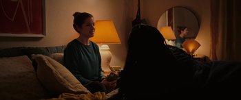 Movie still from “Alice, Darling” (2022), directed by Mary Nighy – A woman sitting on a couch holding a cell phone; Medium shot, Over the shoulder angle