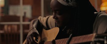 Movie still from “Alice, Darling” (2022), directed by Mary Nighy – A person playing a guitar in a room; Close Up shot, Low angle