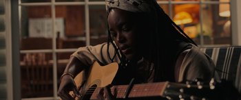 Movie still from “Alice, Darling” (2022), directed by Mary Nighy – A person that is sitting down with a guitar; Close Up shot, Over the shoulder angle