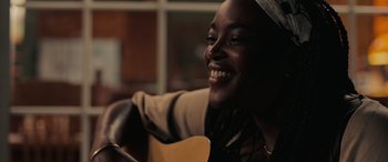 Movie still from “Alice, Darling” (2022), directed by Mary Nighy – A woman smiles while holding a guitar in her hand; Close Up shot, Over the shoulder angle