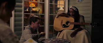 Movie still from “Alice, Darling” (2022), directed by Mary Nighy – Two women sitting on a chair with a guitar; Medium shot, Over the shoulder angle