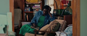 Movie still from “Alice, Darling” (2022), directed by Mary Nighy – A woman sitting on a couch looking at a book; Medium shot, High angle