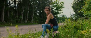 Movie still from “Alice, Darling” (2022), directed by Mary Nighy – A woman sitting on the side of the road in the grass; Medium shot, High angle