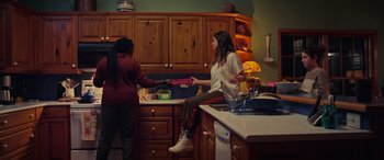 Movie still from “Alice, Darling” (2022), directed by Mary Nighy – Two women in a kitchen one is sitting on the counter and the other is standing up; Wide shot, Over the shoulder angle