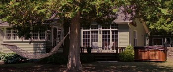 Movie still from “Alice, Darling” (2022), directed by Mary Nighy – A tree in front of a house with a porch and lawn chairs; Wide shot, High angle