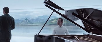 Movie still from “Alien: Covenant” (2017), directed by Ridley Scott – A man standing at a piano in front of a body of water; Medium shot, Low angle