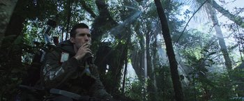 Movie still from “Alien: Covenant” (2017), directed by Ridley Scott – A man sitting in the middle of a forest smoking a cigarette; Medium shot, Low angle