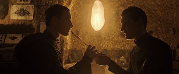 Movie still from “Alien: Covenant” (2017), directed by Ridley Scott – Two men are holding hands in front of a cave; Close Up shot, Over the shoulder angle