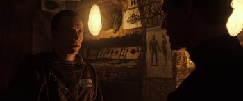 Movie still from “Alien: Covenant” (2017), directed by Ridley Scott – A man standing next to a wall in a dimly - lit room; Medium shot, Over the shoulder angle