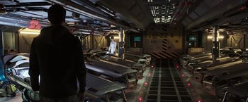 Movie still from “Alien: Covenant” (2017), directed by Ridley Scott – A man standing next to a bunch of metal parts; Wide shot, High angle