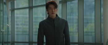 A man in a gray jacket standing in front of a window