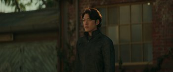 A man in a black jacket standing in front of a brick building