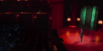 Movie still from “All About Gila” (2022), directed by Arturo González-Campos – A view of a stage with lights and people in it; Extreme Wide shot, High angle