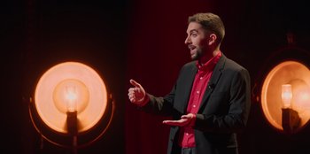 Movie still from “All About Gila” (2022), directed by Arturo González-Campos – A man standing in front of an orange light; Medium shot, High angle