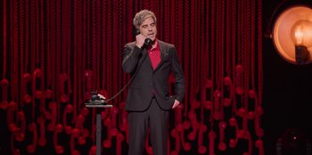 Movie still from “All About Gila” (2022), directed by Arturo González-Campos – A man in a suit and red shirt talking on a phone; Medium shot, High angle