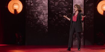 Movie still from “All About Gila” (2022), directed by Arturo González-Campos – A woman standing on a stage in front of a crowd; Wide shot, Over the shoulder angle