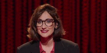 Movie still from “All About Gila” (2022), directed by Arturo González-Campos – A person wearing glasses and a suit; Close Up shot, High angle