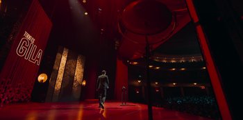 Movie still from “All About Gila” (2022), directed by Arturo González-Campos – A man in a suit is walking in a red room; Extreme Wide shot, High angle