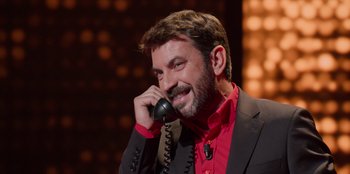Movie still from “All About Gila” (2022), directed by Arturo González-Campos – A man talking on a phone while wearing a suit and red shirt; Close Up shot, High angle