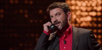 Movie still from “All About Gila” (2022), directed by Arturo González-Campos – A man talking on a phone while wearing a suit and red shirt; Close Up shot, High angle