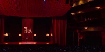 Movie still from “All About Gila” (2022), directed by Arturo González-Campos – A stage lit up with lights and a man on a stage; Extreme Wide shot, Low angle