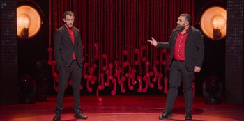 Movie still from “All About Gila” (2022), directed by Arturo González-Campos – A couple of men standing next to each other on a stage; Wide shot, High angle