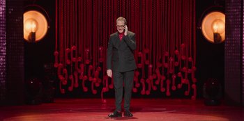 Movie still from “All About Gila” (2022), directed by Arturo González-Campos – A man standing on a stage while talking on a cell phone; Extreme Wide shot, High angle