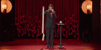 Movie still from “All About Gila” (2022), directed by Arturo González-Campos – A woman in a black suit holding up a wooden stick; Medium shot, High angle