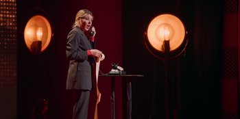 Movie still from “All About Gila” (2022), directed by Arturo González-Campos – A woman standing on a stage talking on the phone; Medium shot, Low angle