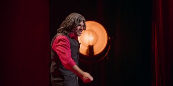 Movie still from “All About Gila” (2022), directed by Arturo González-Campos – A man in a red shirt and black vest holding a microphone; Medium shot, Low angle