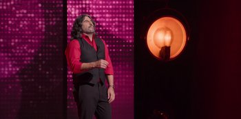 Movie still from “All About Gila” (2022), directed by Arturo González-Campos – A man standing on a stage in front of a microphone; Medium shot, Low angle