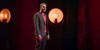 Movie still from “All About Gila” (2022), directed by Arturo González-Campos – A man standing in front of a lamp in a dark room; Medium shot, Low angle