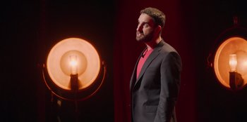 Movie still from “All About Gila” (2022), directed by Arturo González-Campos – A man standing in front of a light in a dark room; Medium shot, Low angle